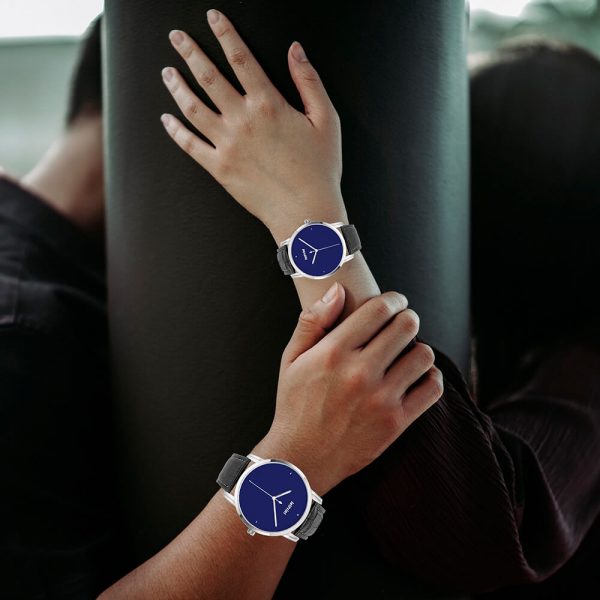 A man and a woman each have a dark blue watch on their hands and are leaning against a wall.