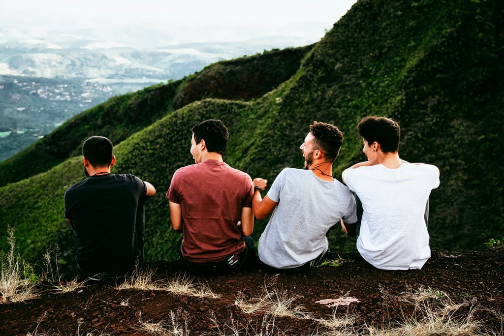 four men in t-shirts sitting on top of a mountain