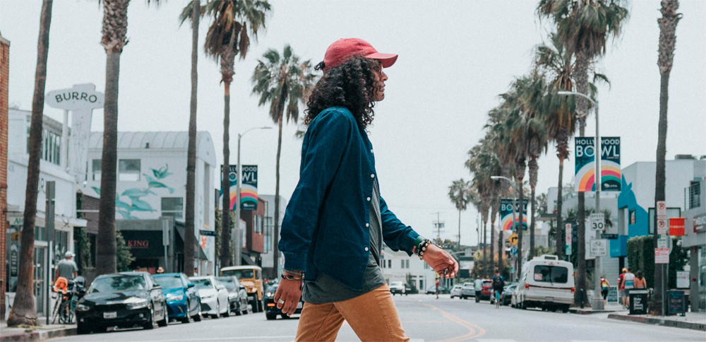 A man wearing a red cap is crossing the road