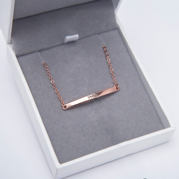 A rose gold-tone text bracelet is housed in a jewelry box