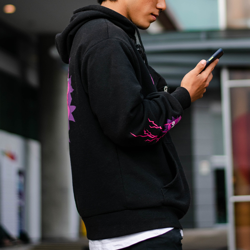 A man wearing a black AOP hoodie is playing with his phone.