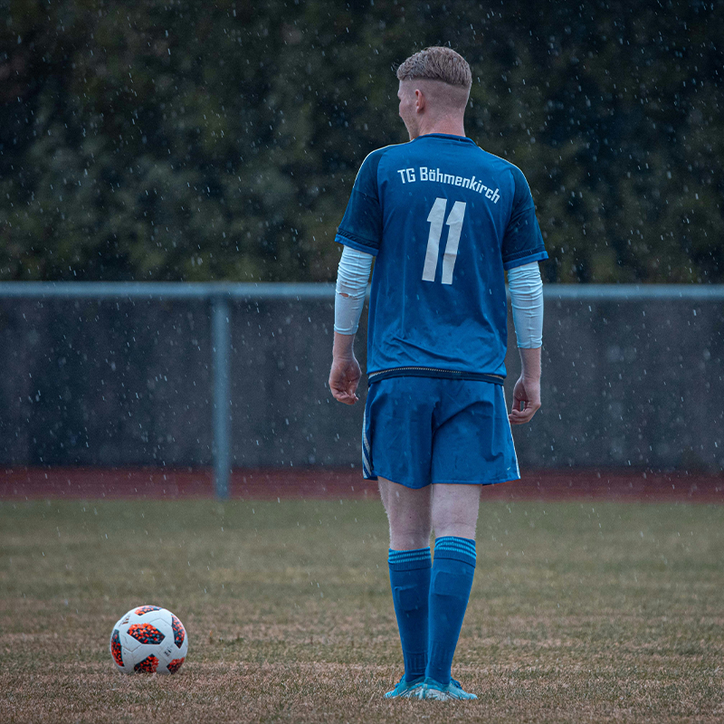 An athlete in a blue soccer jersey plays soccer on the field