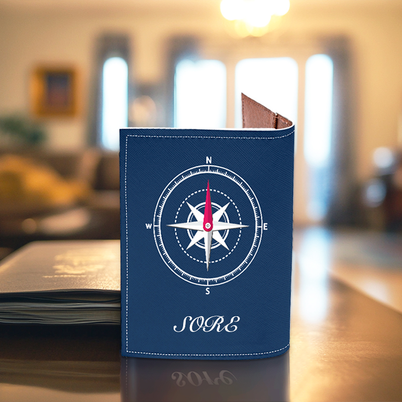 A blue passport cover with a compass logo and name on it is placed on a table