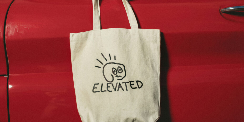 A tote bag with a hand-painted design is hung on a red car