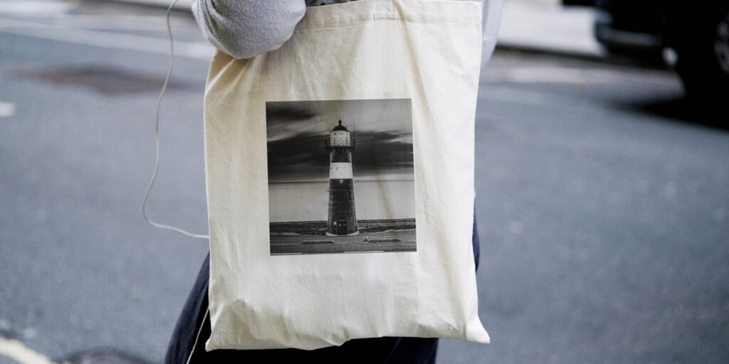 A woman holds a tote bag with a black and white lighthouse picture