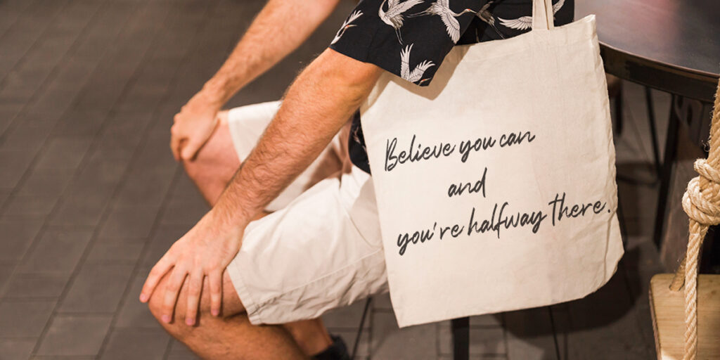 A man carries a tote bag with a motivational quote