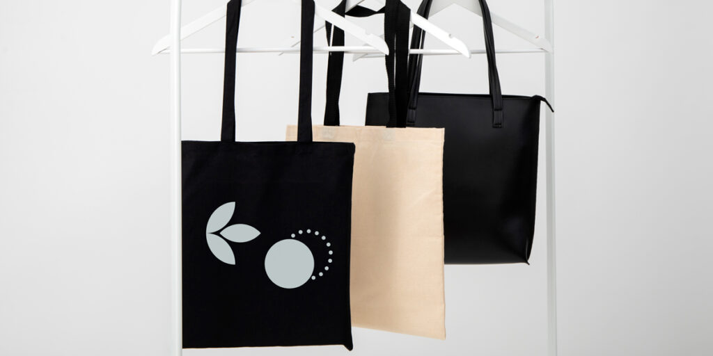 Three simple tote bags are hung on a hanger